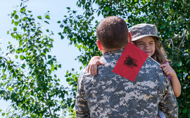 Reunion of soldier from Albania with family, daughter hug father. A girl holds the flag of Albania in her hand