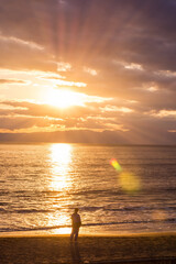 A silhouette man is standing lonely sightseeing for the sunset over the sea and beach. The photo presented of recreation and summer time in tropical and asian country. Taken with flare effect.