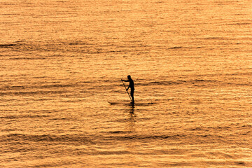 Fototapeta na wymiar silhouette of lonely man kayaking alone during on the sea level during sunset taking in warm and orange tone.