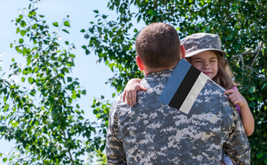 Reunion of soldier from Estonia with family, daughter hug father. A girl holds the flag of Estonia...