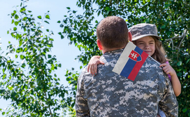 Reunion of soldier from Slovakia with family, daughter hug father. A girl holds the flag of...
