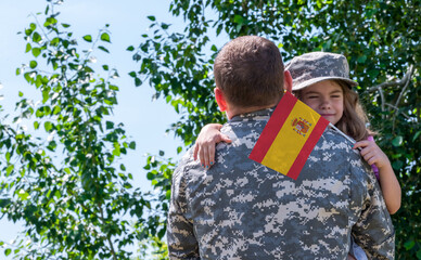 Reunion of soldier from Spain with family, daughter hug father. A girl holds the flag of Spain in...