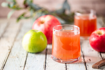Glass of fresh apple juice and red apples on wooden background