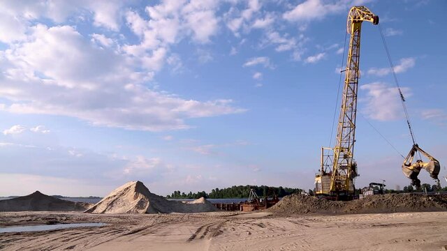 Sand mining near the river. A crane with a bucket unloads wet sand