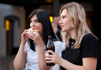 Pretty young women eating hamburger and drink beer outdoor on the street