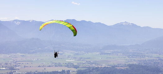Adventurous Woman Flying on a paraglider around the Canadian Mountain Landscape. Harrison Mills near Chilliwack, British Columbia, Canada.