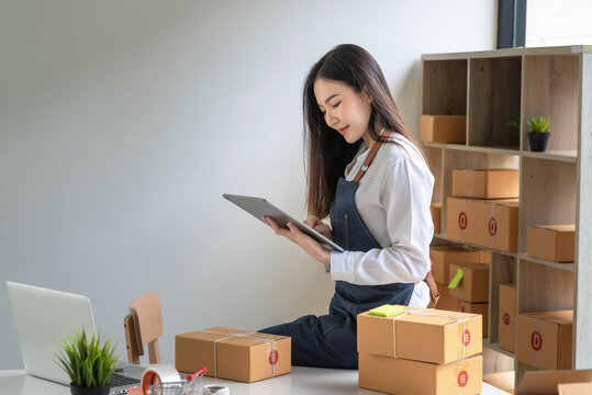 Asian Woman Small Business Owner Holding A Tablet To Check Parcels Before Delivering To Customers At Home.