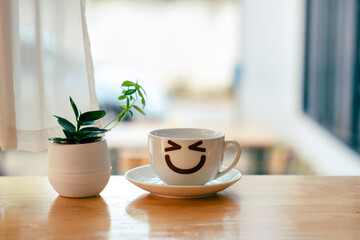 Happy smiley coffee cup with a flowerpot on the table.