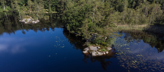 Bird's eye view of a pond, lake with green trees. Aerial, drone nature photography taken from above in Sweden in summer. Wide panorama banner with copy space and place for text.