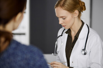 Friendly smiling female doctor and patient woman discussing current health examination while...