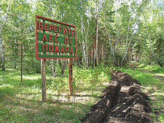 Protective strip from the fire in the forest. The inscription on the signpost in Russian "Protect the forest from fire".