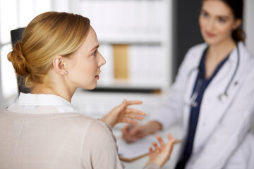 Fototapeta premium Friendly smiling female doctor and patient woman discussing current health examination while sitting in clinic. Perfect medical service in hospital. Medicine concept