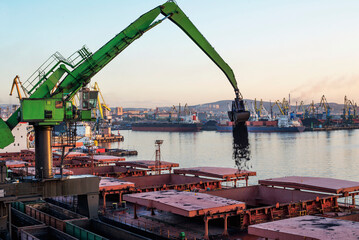 A manipulator crane in the seaport is used for unloading wagons and loading bulk cargo into the holds of sea ships.