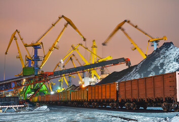 Twilight. Heaps of coal in the seaport. Coal is unloaded from wagons by all kinds of cranes, then loaded into the holds of sea ships.