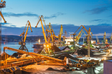 Twilight. Heaps of coal in the seaport. Coal is unloaded from wagons by all kinds of cranes, then loaded into the holds of sea ships.