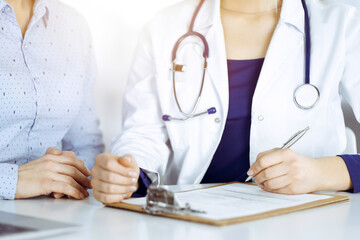 Young beautiful woman-doctor and her patient are discussing patient's current health examination,...