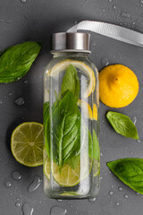 Infused water with lemon, lime and basil in a transparent glass bottle on a gray background close-up. Health and wellness concept.