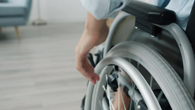 Close-up slow motion of woman's hand moving wheelchair indoors at home while female paraplegic is busy with domestic activities. Disability and mobility concept.