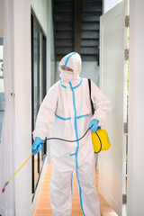 A medical staff in PPE suit is using disinfectant spray in living room, Covid-19 protection , disinfection concept .