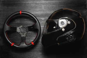 Car sport steering wheel and rally helmet on the black flat lay background. Motorsport concept.
