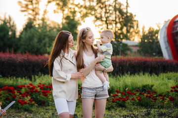 A young homosexual family of mothers hugs and plays in the park with their young son during sunset. Modern happy lesbian family.