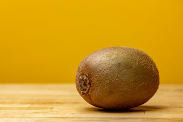 Texture close up of fuzzy kiwifruit with brown hair-like peel on a light wooden counter  surface contrasted against a light yellow studio background. Food Still life.