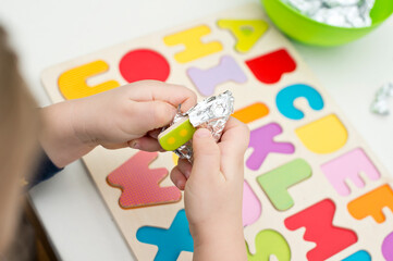 Two year boy playing with wooden alphabet letters board. Letters wrapped in foil. Intellectual game, preschool implement for early education. Verbal and memory training exercise.