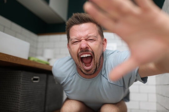 Man sitting on toilet and screaming in pain