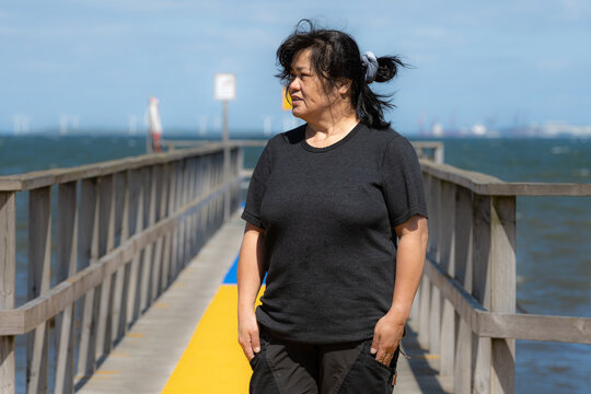 An Asian middle aged woman on a jetty with a yellow and blue carpet and a blue ocean and sky in the background. Picture from Scania county, Sweden