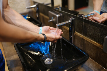 Man washing his hands under running water from tap in public toilet closeup
