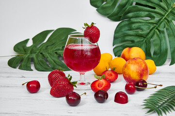 A glass of red drink. Sweet cherries, apricots, peaches and strawberries on a light background. Healthy eating. Healthy drinks. Vitamins.