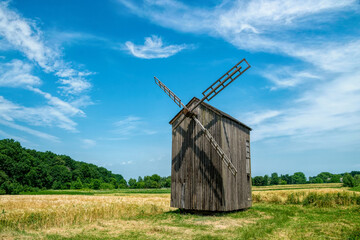 Fototapeta na wymiar Old abandoned wooden mill and wheat summer field