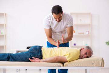 Obraz na płótnie Canvas Old male patient visiting young male doctor chiropractor