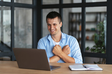 Fototapeta premium Online communication. Handsome caucasian young male freelancer or student uses sign language while video call using laptop while sitting at home office