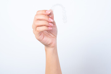 Woman's hand with pink manicure holding an invisible aligner braces. Dental healthcare concept. 