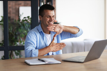 Happy smiling deaf young caucasian man uses sign language while video call using laptop while sitting at home, virtual communication concept