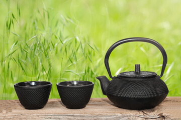 traditional oriental cast iron teapot and two cups of hot tea on an old wooden surface on a green...
