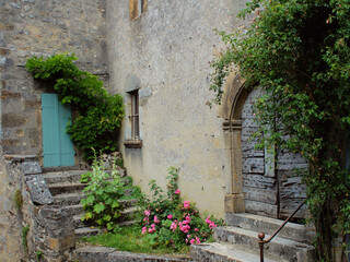 Fototapeta na wymiar Fresh green plants and flowers around rustic old doors of charming country-style grey stone medieval houses in Vezelay village, Burgundy, France, a popular European tourist destination.