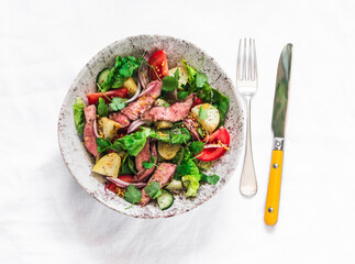 Potato, beef steak, fresh greens and vegetable salad on a light background, top view. Balanced...