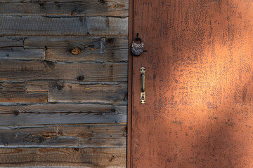 An old brown iron door locked with a padlock. There are foci of rust. Part of the wooden wall with the joining of the timber is visible. Background. Texture.
