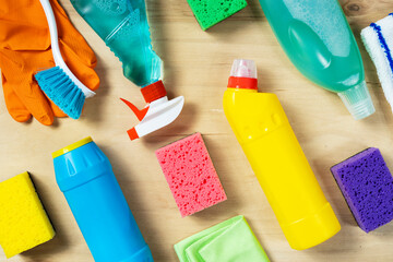 Various cleaning supplies, sprays, bottles, sponge, rubber gloves on wooden background, top view....