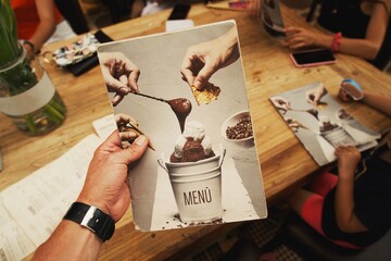 Hands hold a menu of coffee and desserts in a cafe.