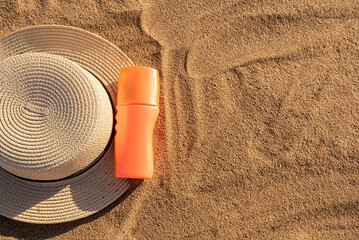 Orange bottle for sunscreen or lotion. Yellow hat. Container with a black shadow on the sand.