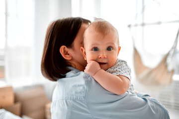 Loving mom carying of her newborn baby at home.Mom and baby boy playing in sunny bedroom. Parent...