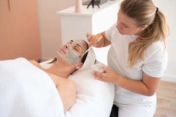 Obraz na płótnie Canvas Cleaning and moisturise nourish skin of face. Cosmetologist put grey mask on face by brush. Beautiful woman receiving cavitation facial peeling. Treatment skin care in cosmetology beauty spa salon.