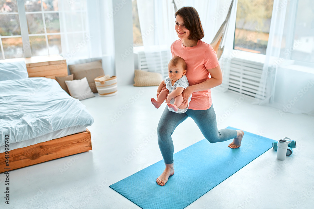 Wall mural A sports mother is engaged with the child in fitness and yoga at home. The concept of sports, motherhood and an active lifestyle. Young woman in sports training with her child.