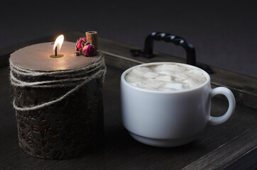 Cup of cappuccino coffee on a wooden table tray. Candle. Breakfast