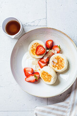 Homemade cottage cheese fritters syrniki with strawberries and maple syrup, Russian and Ukrainian cuisine concept.