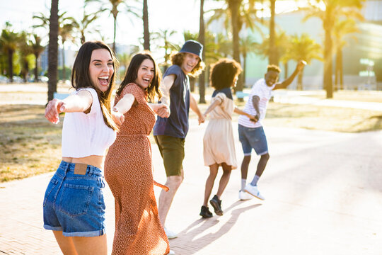 Multiethnic group of young friends running happily together while holding hands - Travel lifestyle concept with multiracial group of millennial tourists having fun in summer 