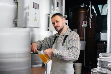 A young bearded brewer conducts quality control of freshly brewed beer in the brewery.